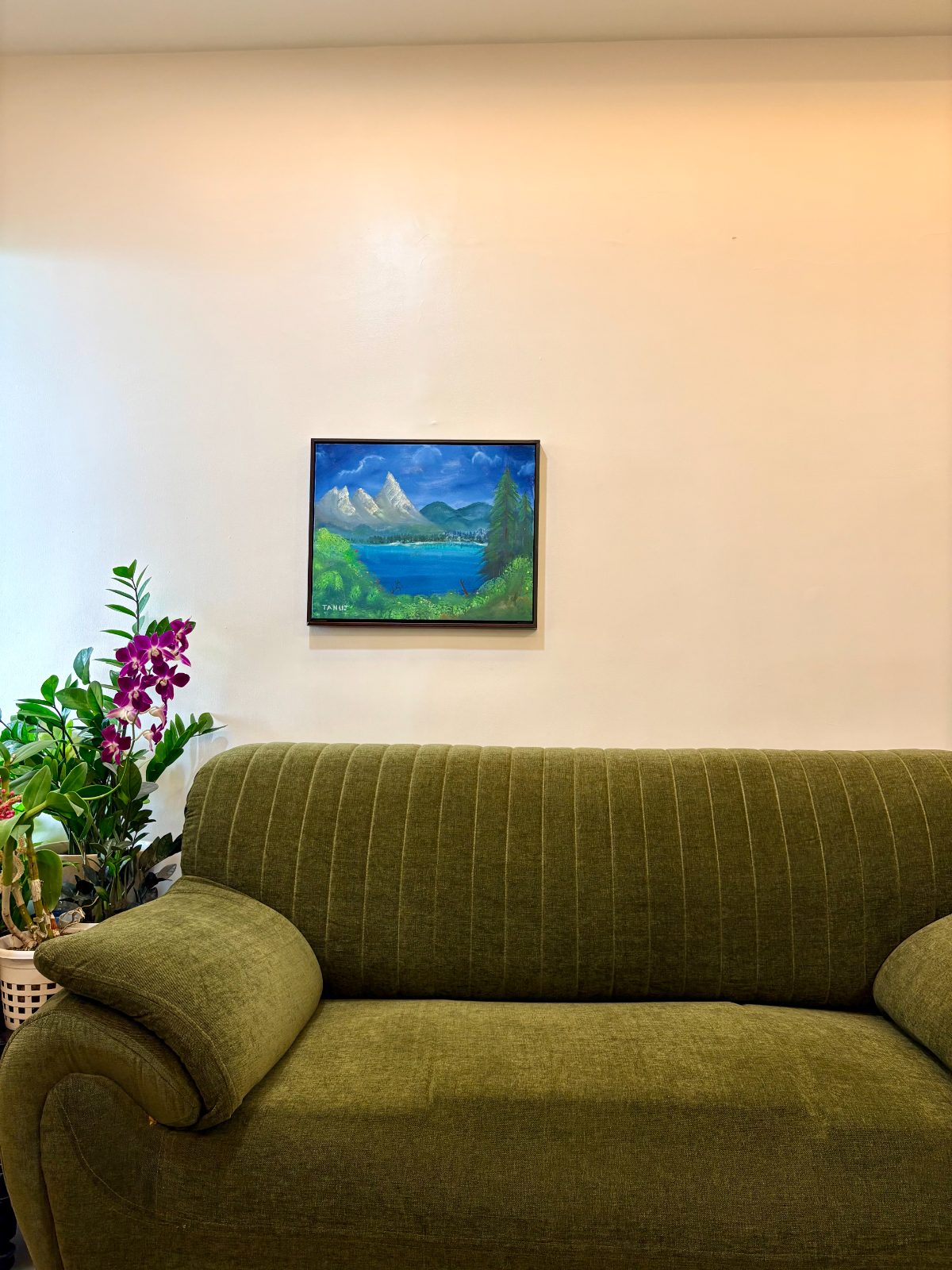 A green velvet couch beneath Tanuj's hand-painted mountain landscape